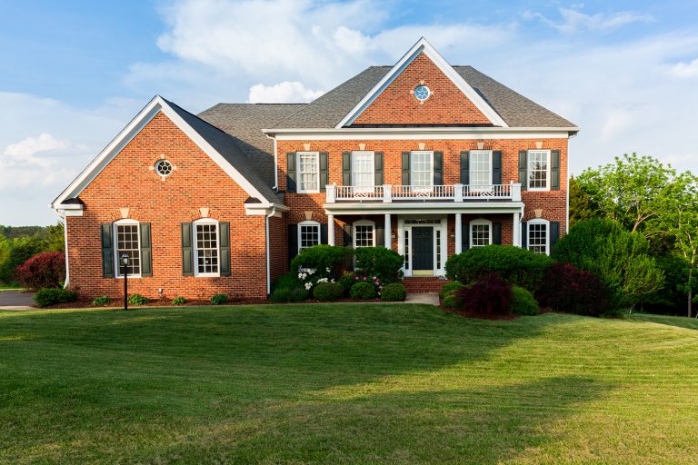 Front of home and garage of large single family modern US house with landscaped gardens and lawn on a warm sunny summers day